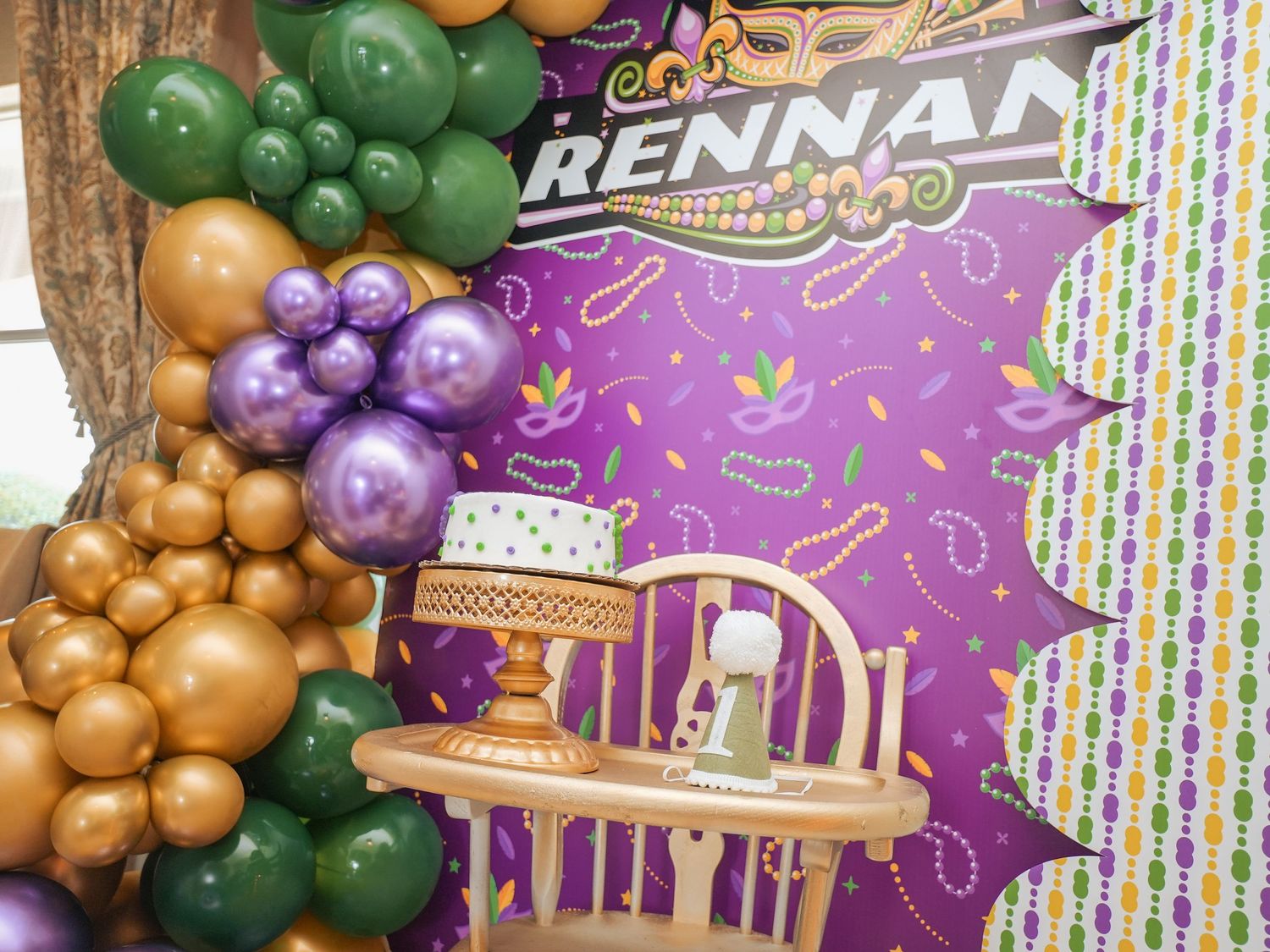 Party backdrop with balloon arch in gold, purple and green with personalized name design.