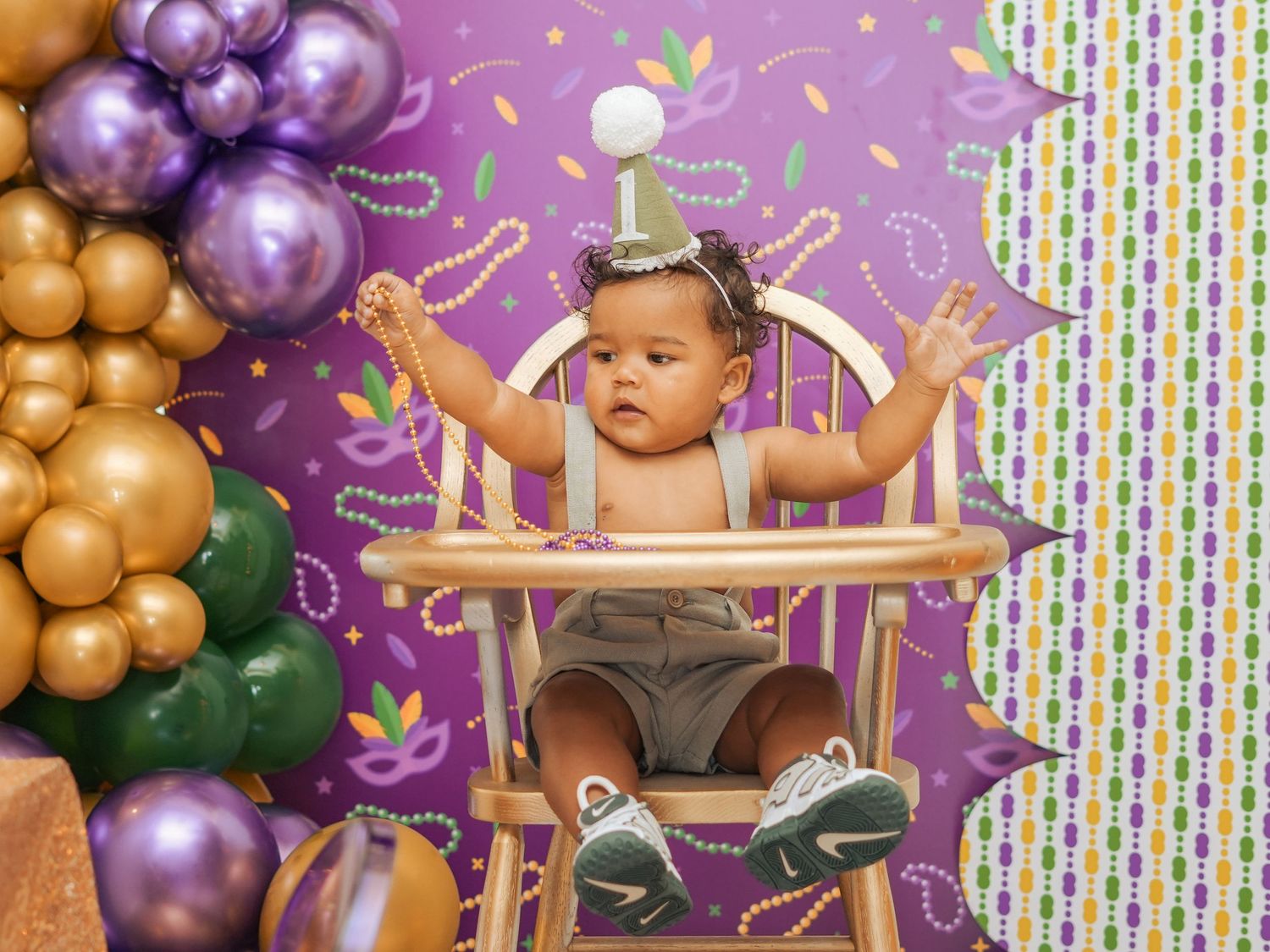 Festive first birthday photo setup with wooden high chair and balloon decorations.
