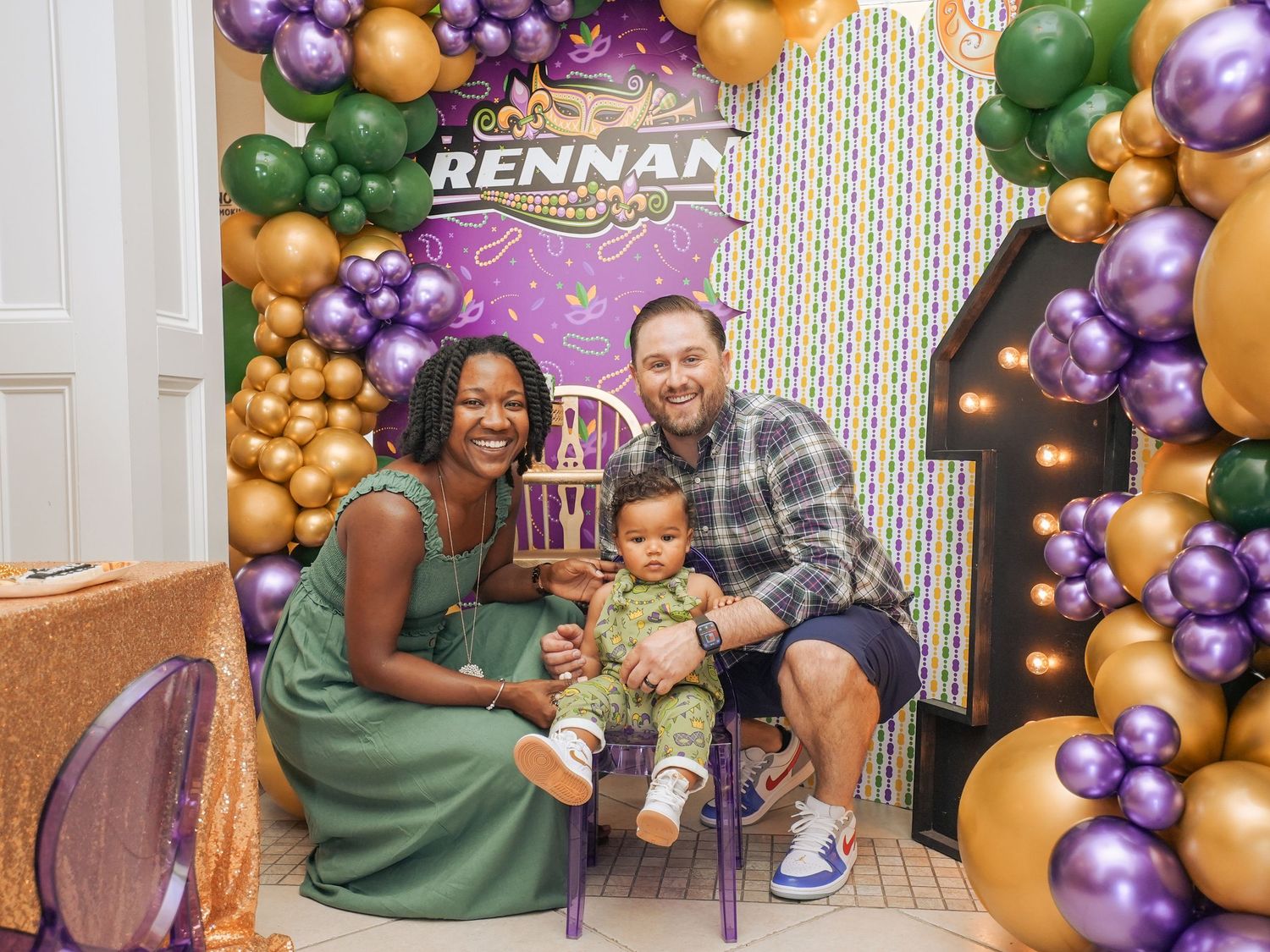 Birthday party setup with custom backdrop and balloon arch in purple, gold and green.