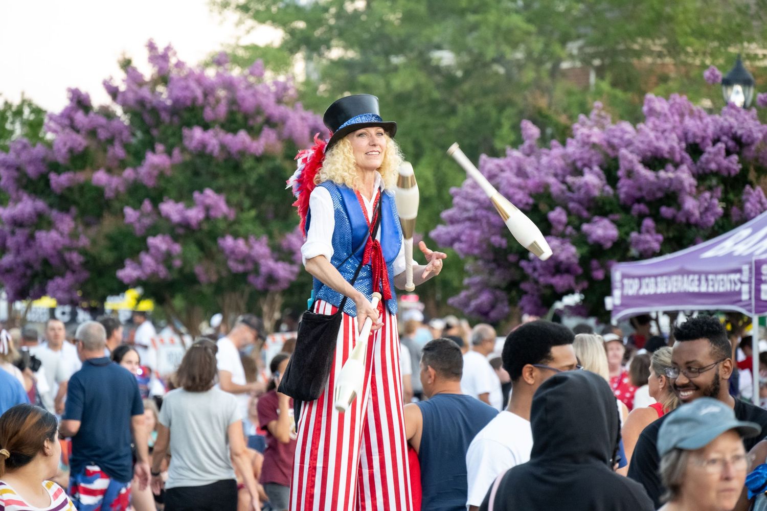 Festive parade performer on stilts wearing patriotic costume among crowd.