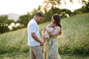 Parents share tender moment with baby in sun-drenched field.