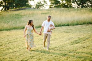Family walks together through grassy field during sunset photoshoot.