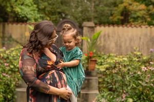 A person in a brown jacket embraces a child wearing a teal raincoat in a lush garden setting.