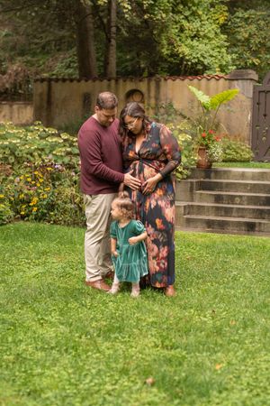 A family shares a tender moment together on a grassy lawn near garden steps in a park setting.
