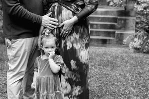 Black and white candid photo of a small child in a dress standing near adults in a garden setting.