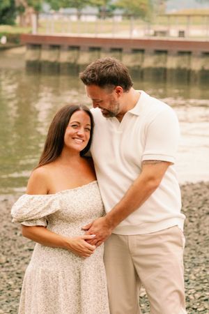 Couple shares tender moment by waterfront wearing coordinating cream and white outfits.