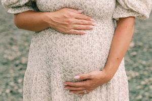 Close-up of hands cradling pregnant belly in cream colored dress.