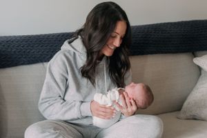 Parent in gray sweatshirt tenderly holding newborn baby on a couch.