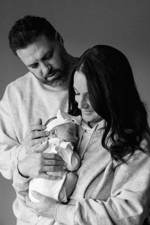 Black and white portrait of parents in matching sweaters holding their newborn.