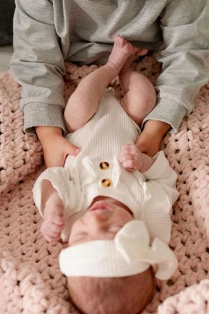 Baby in white outfit lying on pink knitted blanket during playtime.