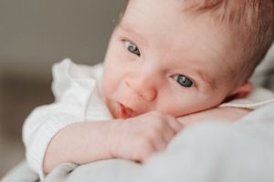 Close-up of baby in white outfit with bright expression.