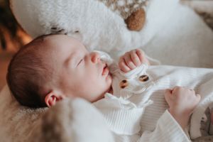 Sleeping newborn in white outfit lying peacefully on soft fabric.