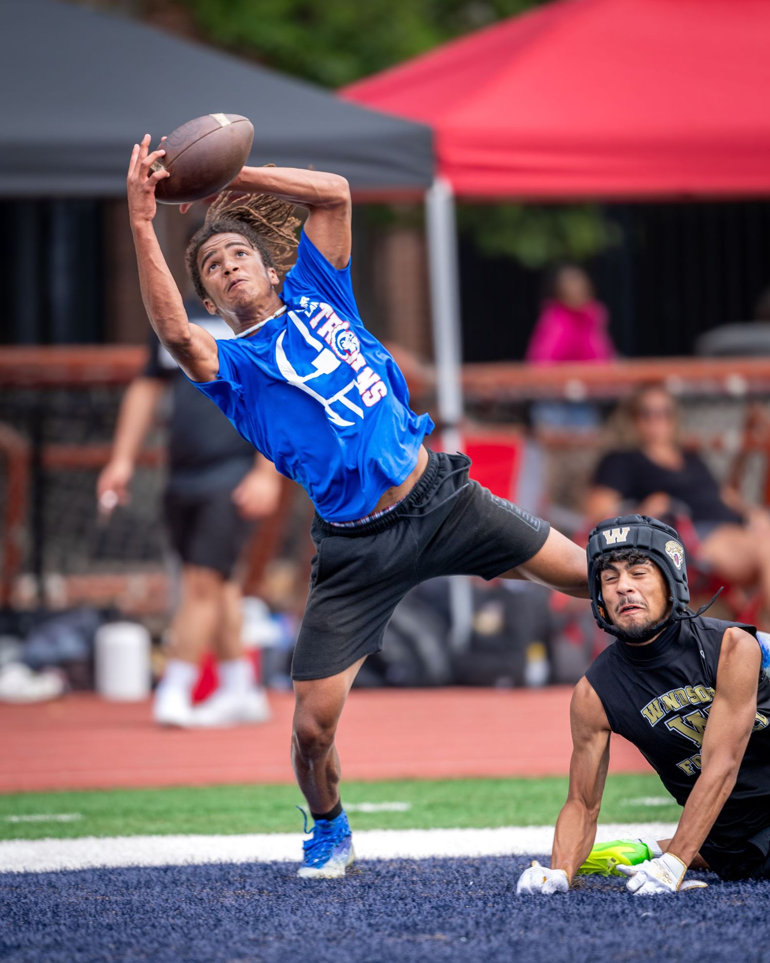 Football player in blue jersey making acrobatic catch attempt in the endzone.