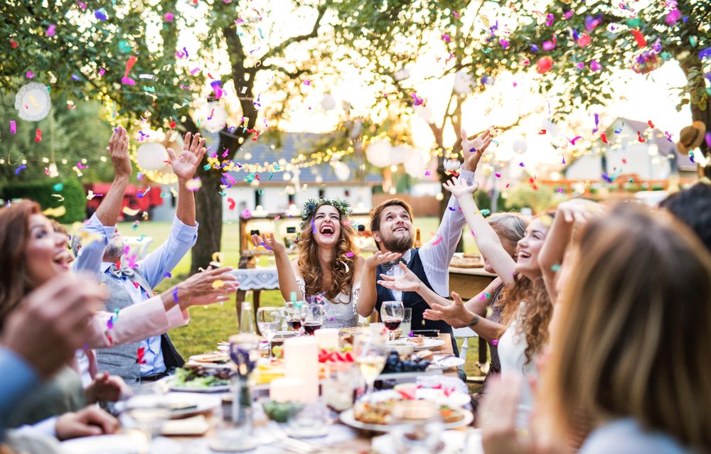 Cheerful outdoor celebration with guests dining at a decorated table under blooming trees.