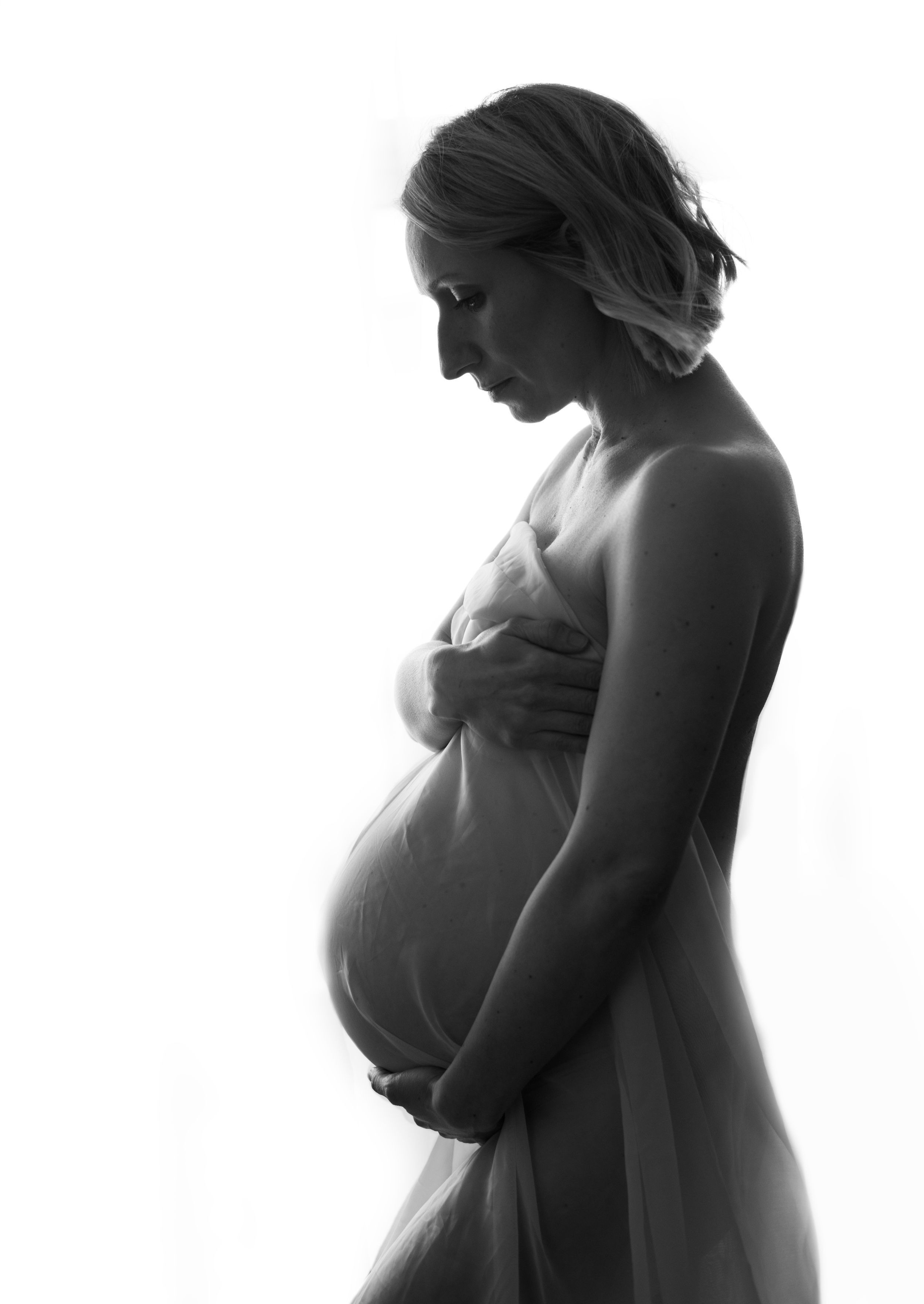 Nude pregnant woman holding her bump with white material
