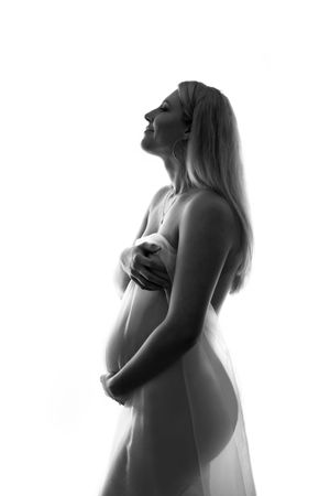 Artistic black and white silhouette of an expectant mother in profile with long hair, standing in soft light.