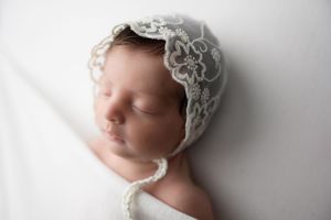 baby girl in a white bonnet tucked in blanket during a newborn portrait session