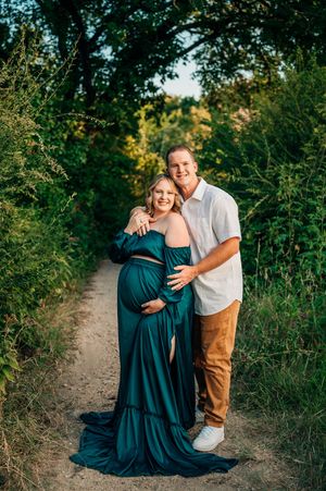 couple snuggled close during maternity leave photoshoot both smiling and looking at camera in Fort Worth park