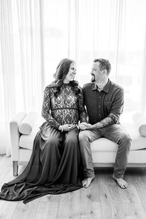 black and white portrait of a couple looking at each other laughing with hands on belly as the woman is pregnant