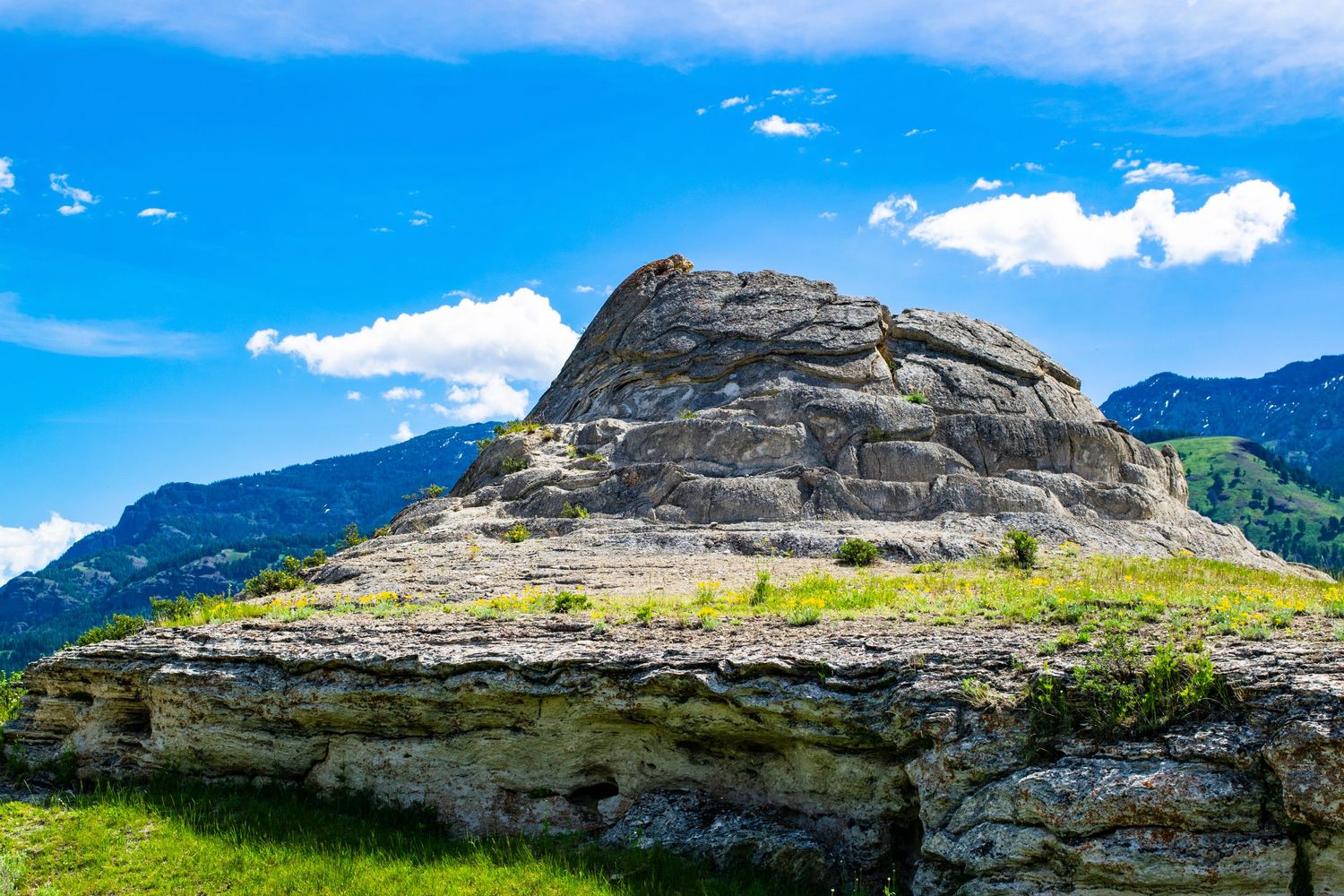Dramatic rock formation rises against blue sky with white clouds in mountainous terrain.