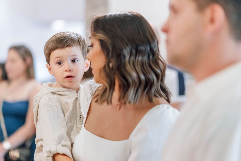 A small child in a beige sweater is being held during a formal event.