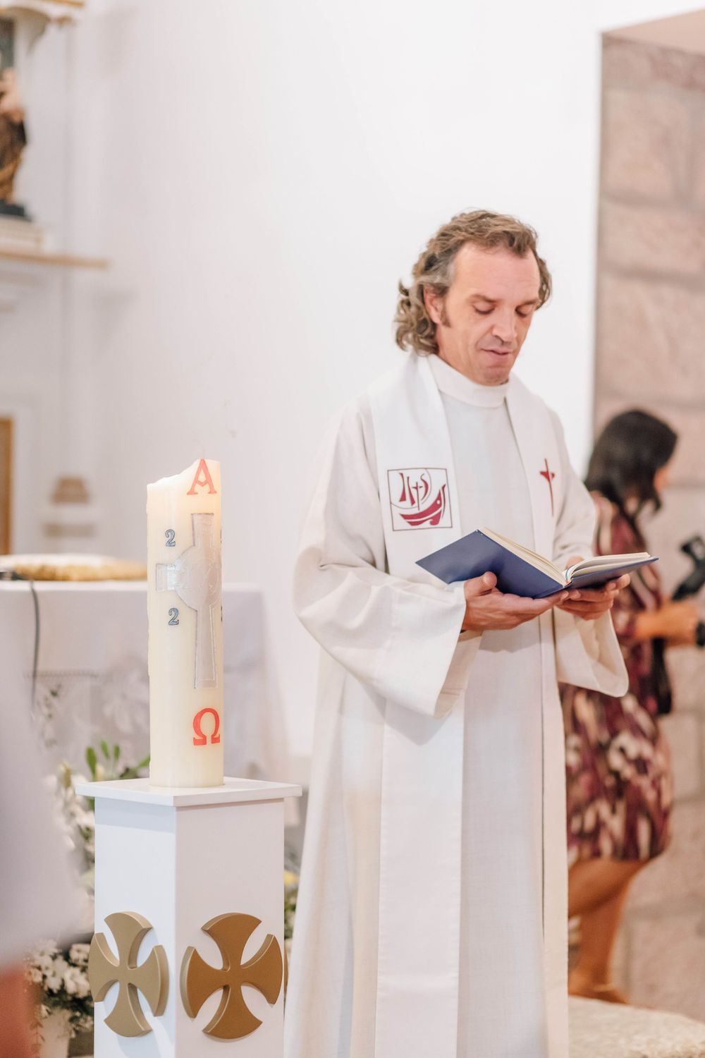 A priest in white robes reading from a book during a religious ceremony.