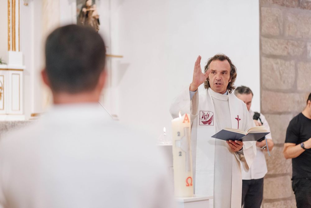 A priest conducting a religious ceremony in a white church interior.