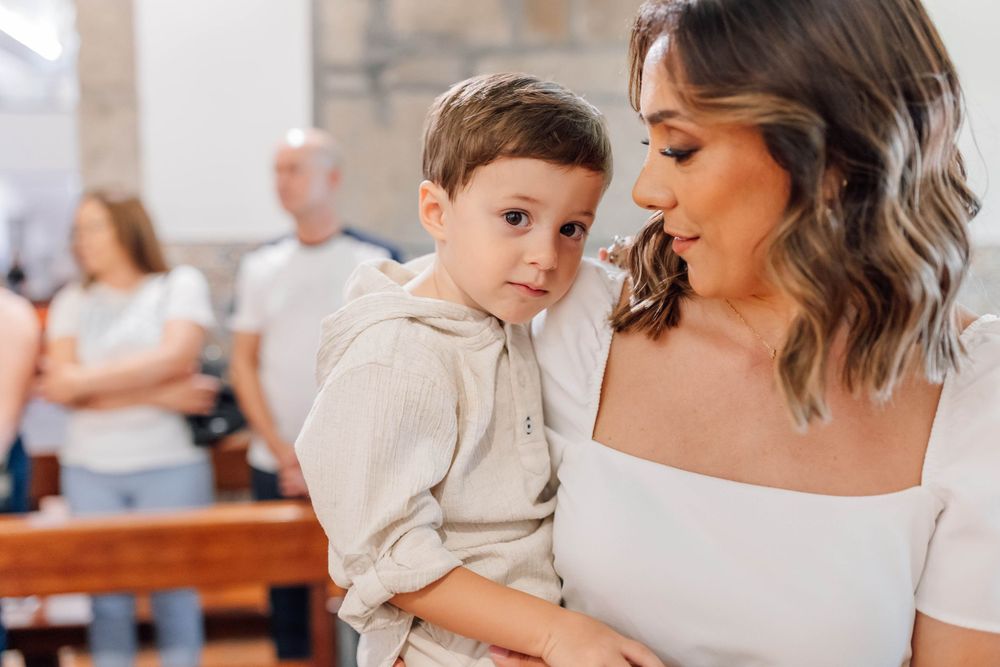 A young child in beige clothing being held at an indoor gathering.