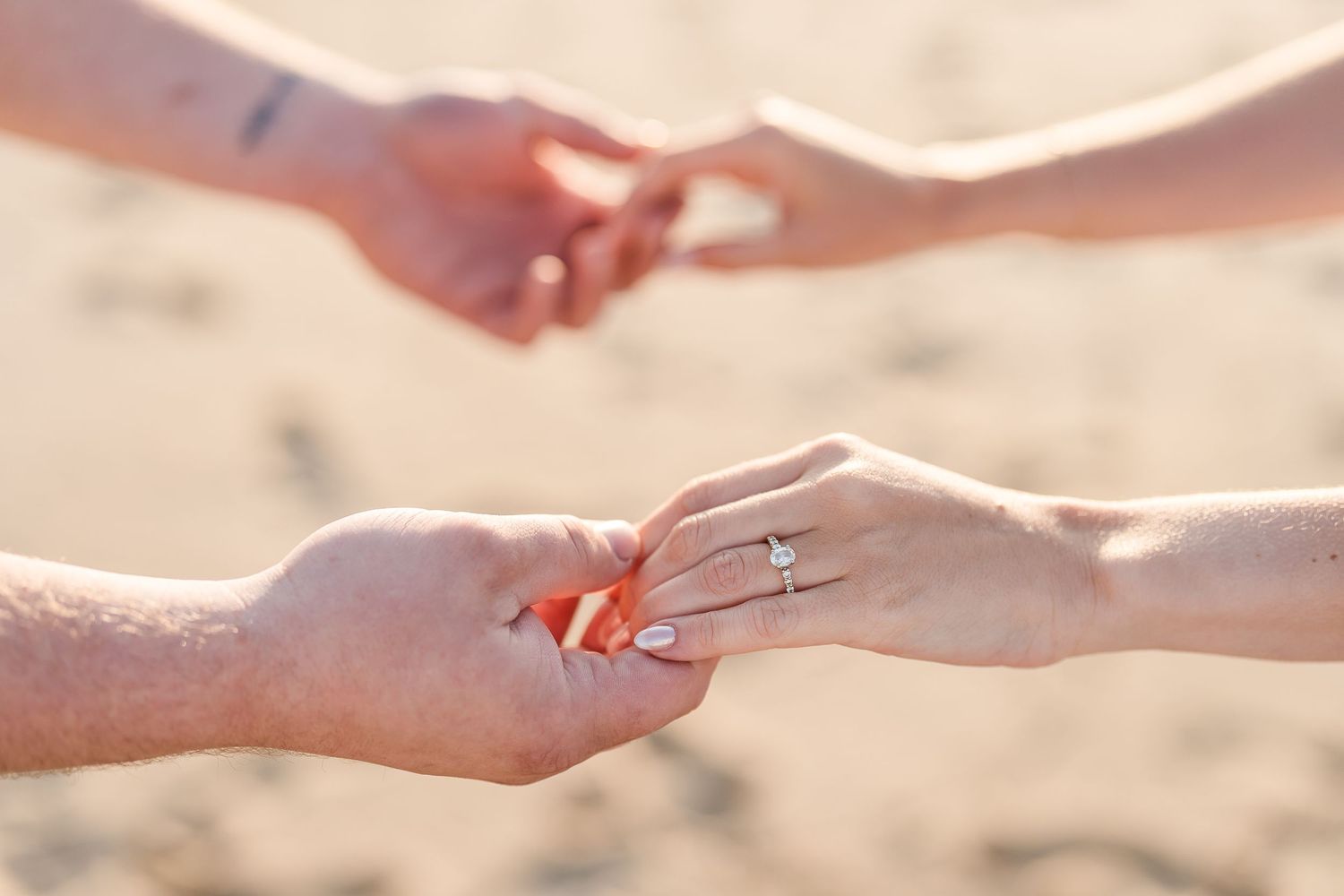 Close-up of couple holding hands on a beach, showcasing a diamond engagement ring.