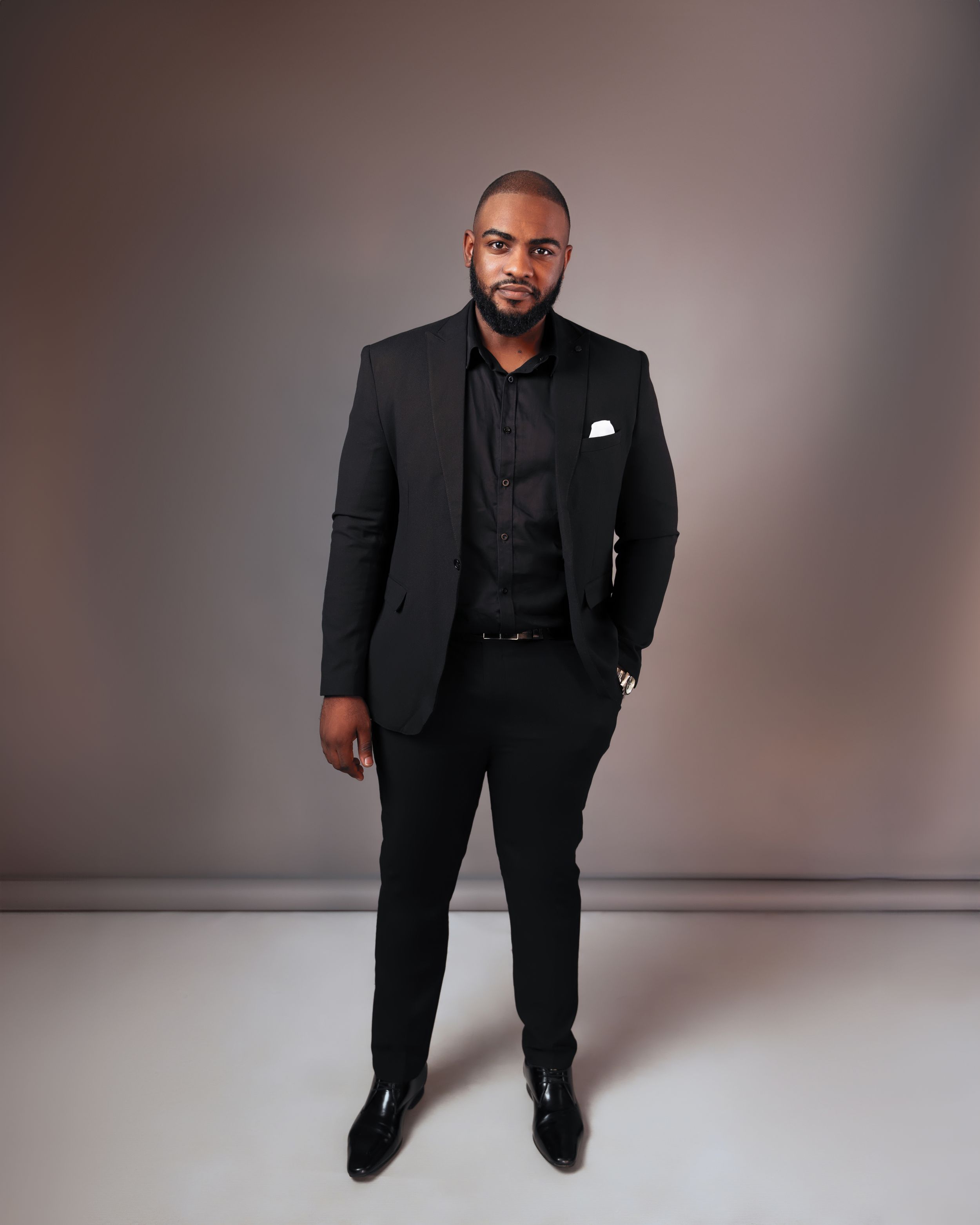 Professional studio portrait in black suit against neutral background.