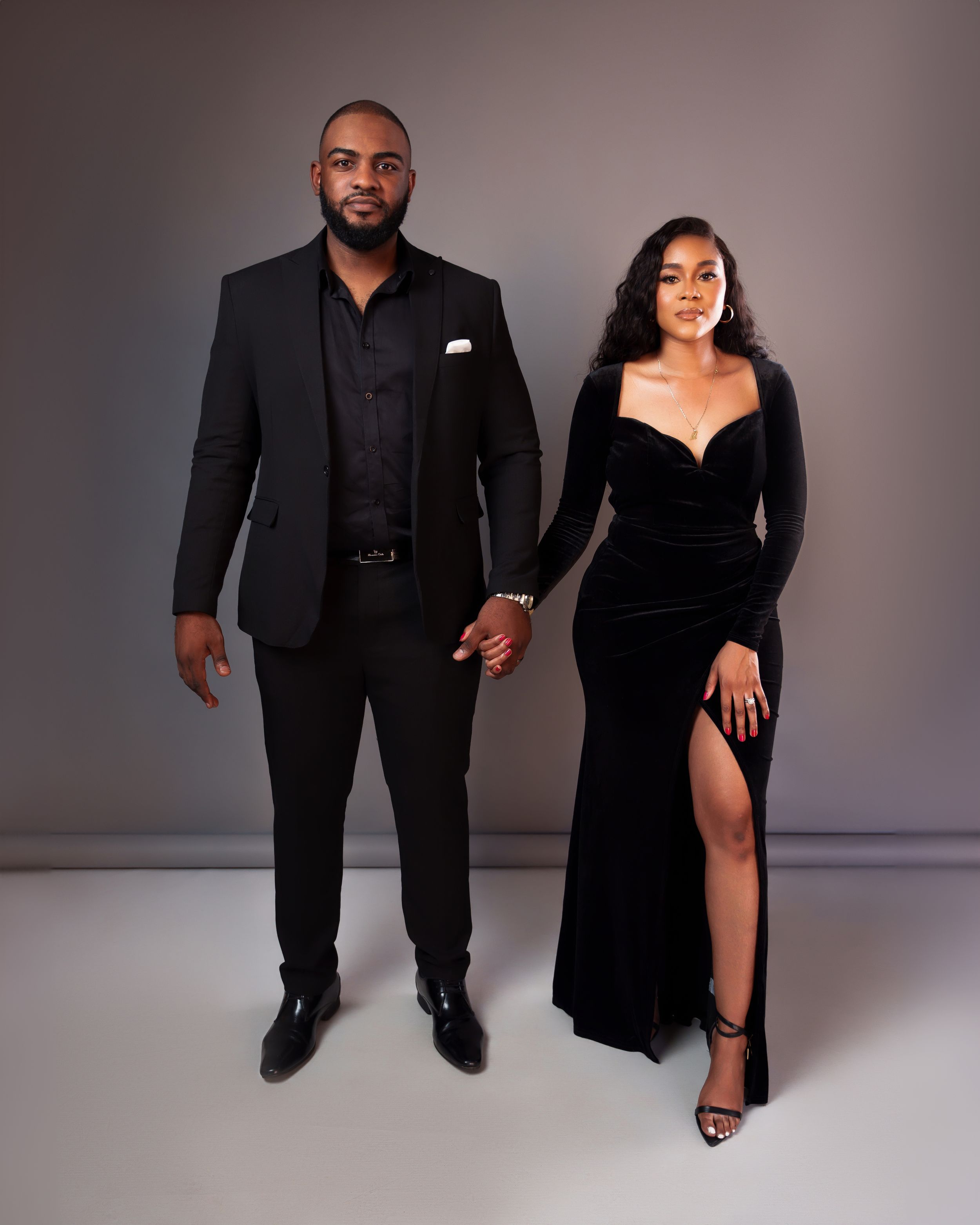Elegant couple in coordinated black formal attire pose together in studio setting.