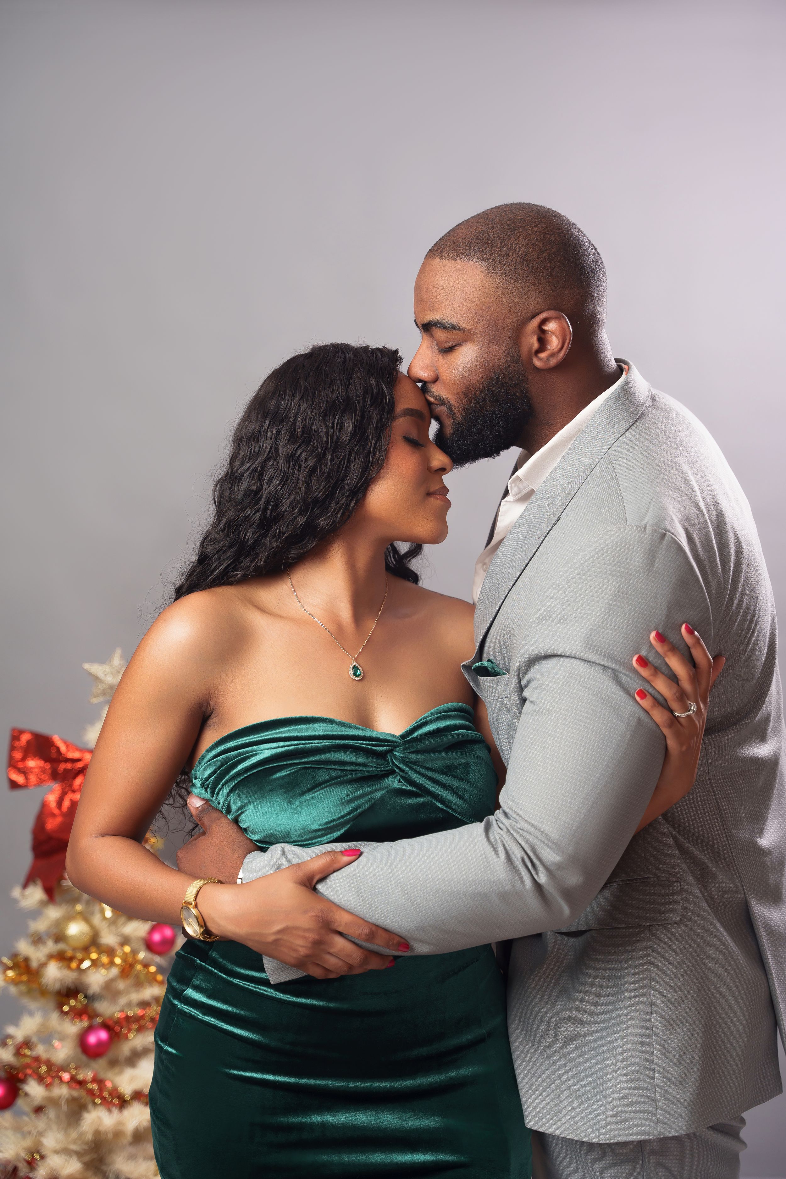 Romantic couple embracing near Christmas decorations with contrasting grey and emerald formal wear.