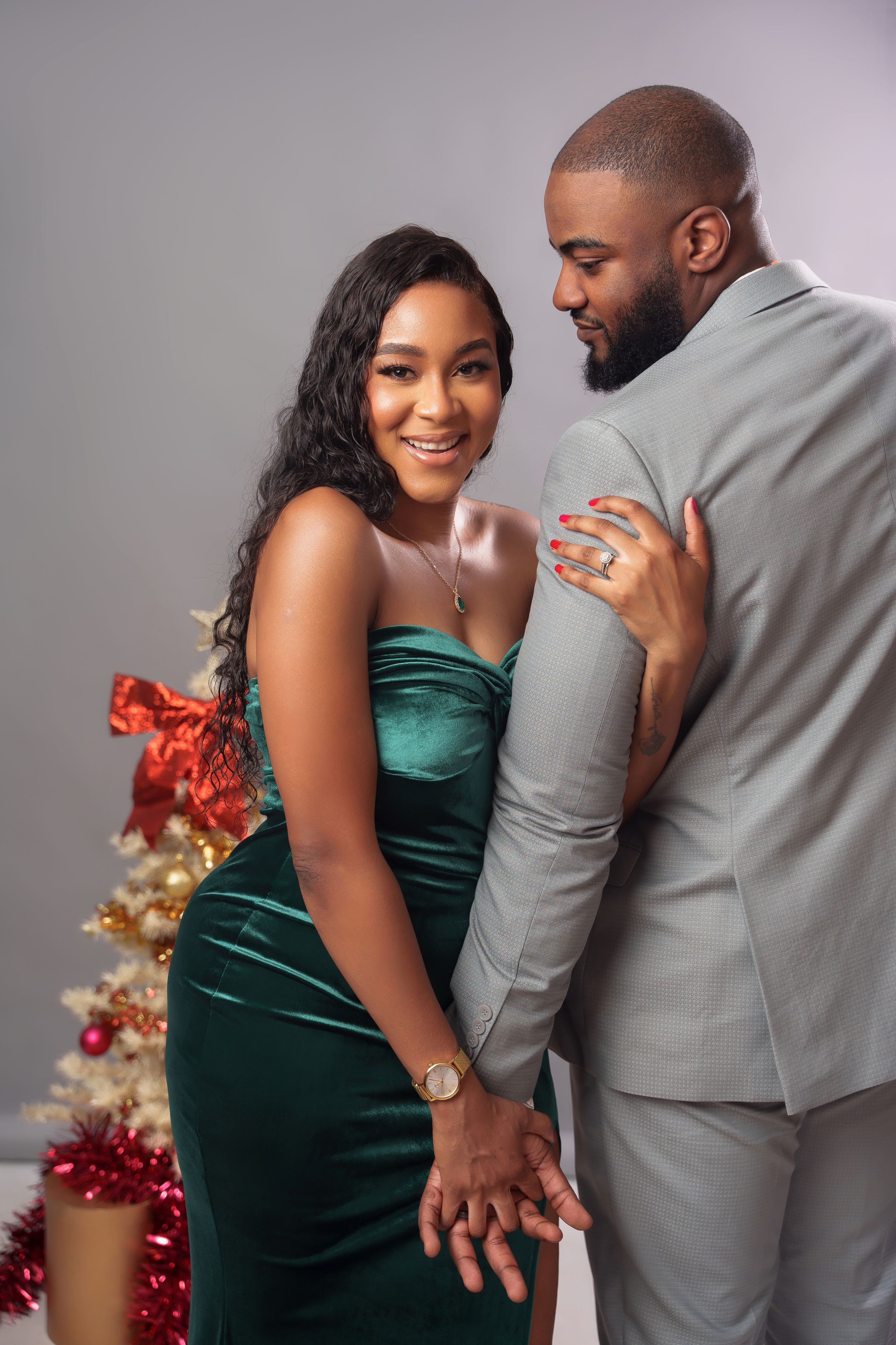 Couple shares tender moment in formal wear near decorated Christmas tree with soft lighting.