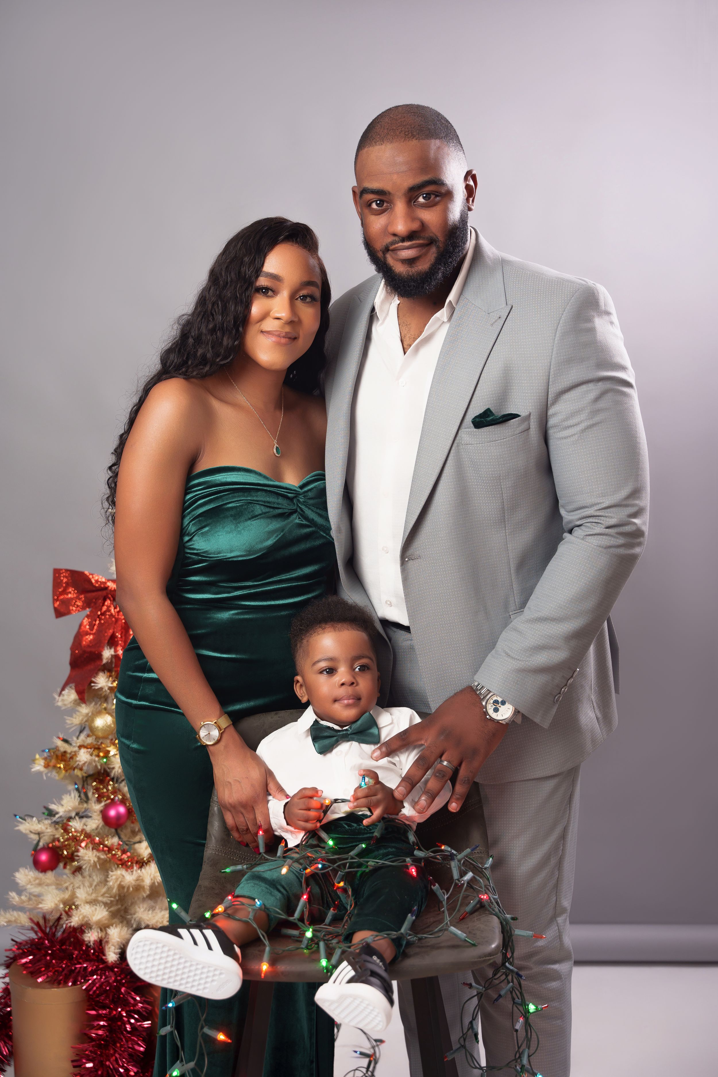 Family holiday portrait with emerald and grey formal wear coordination beside Christmas decorations.