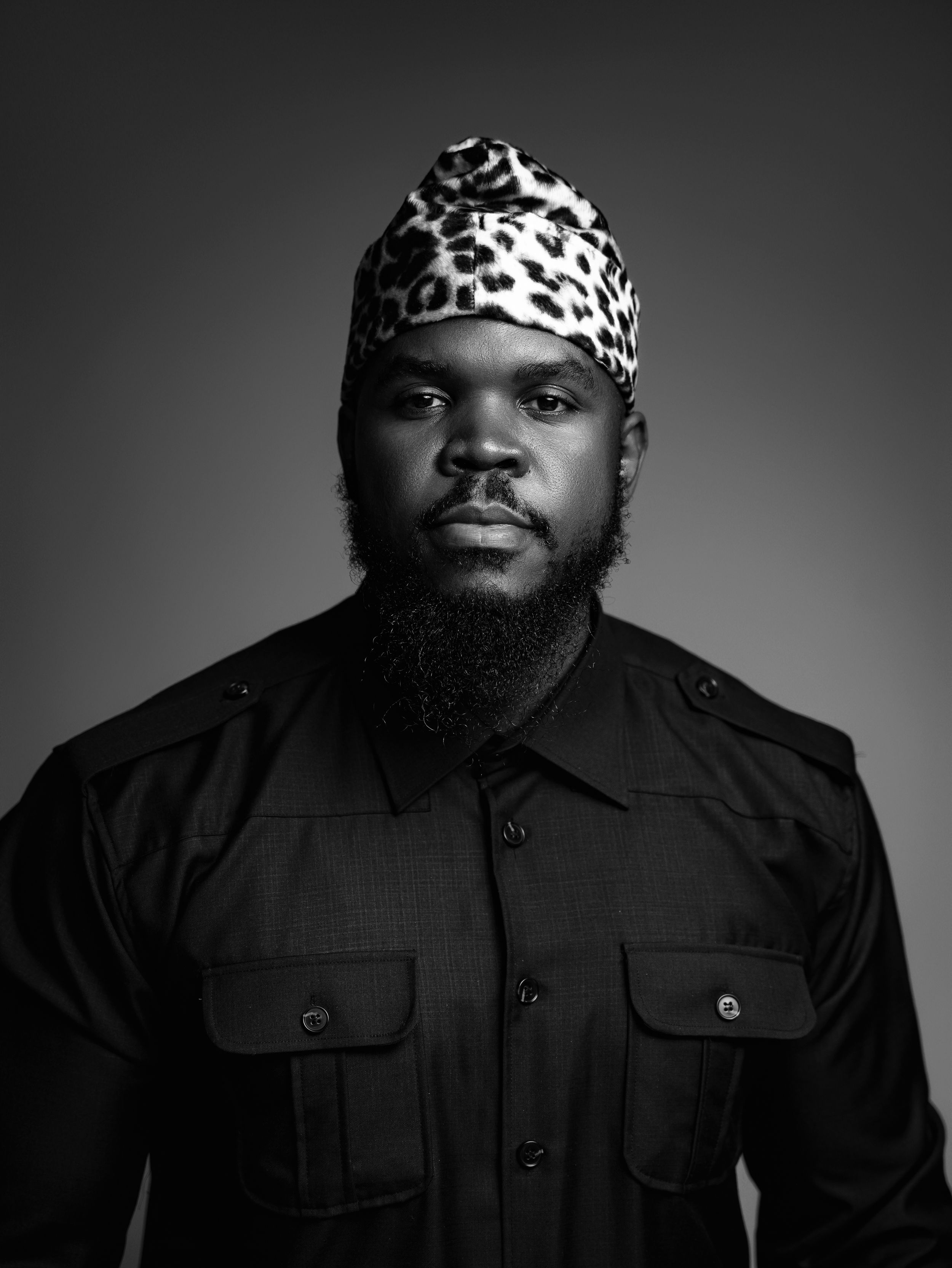 Dramatic black and white portrait with leopard print hat and black button-up shirt.