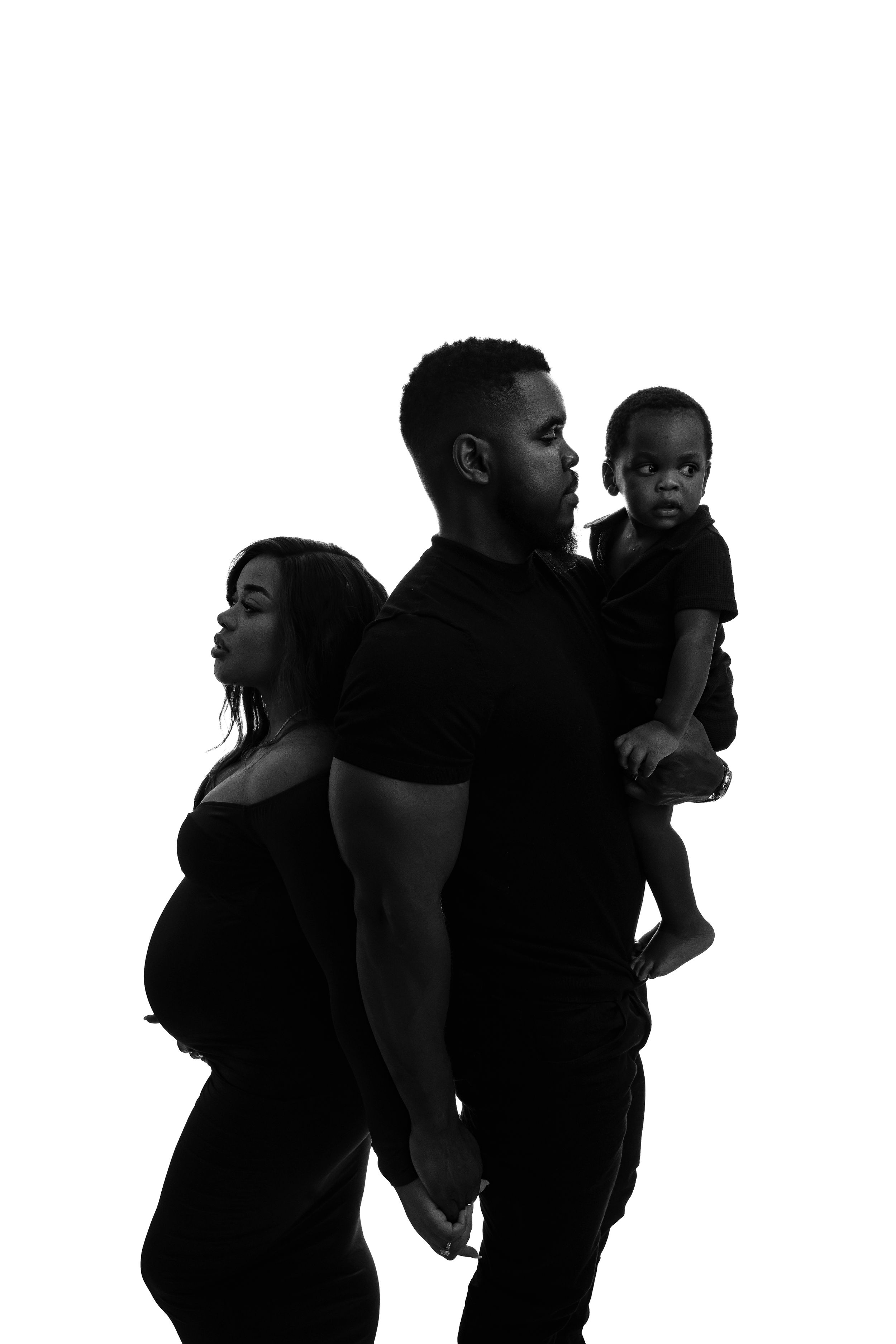 Artistic silhouette of expecting family with toddler against white background.