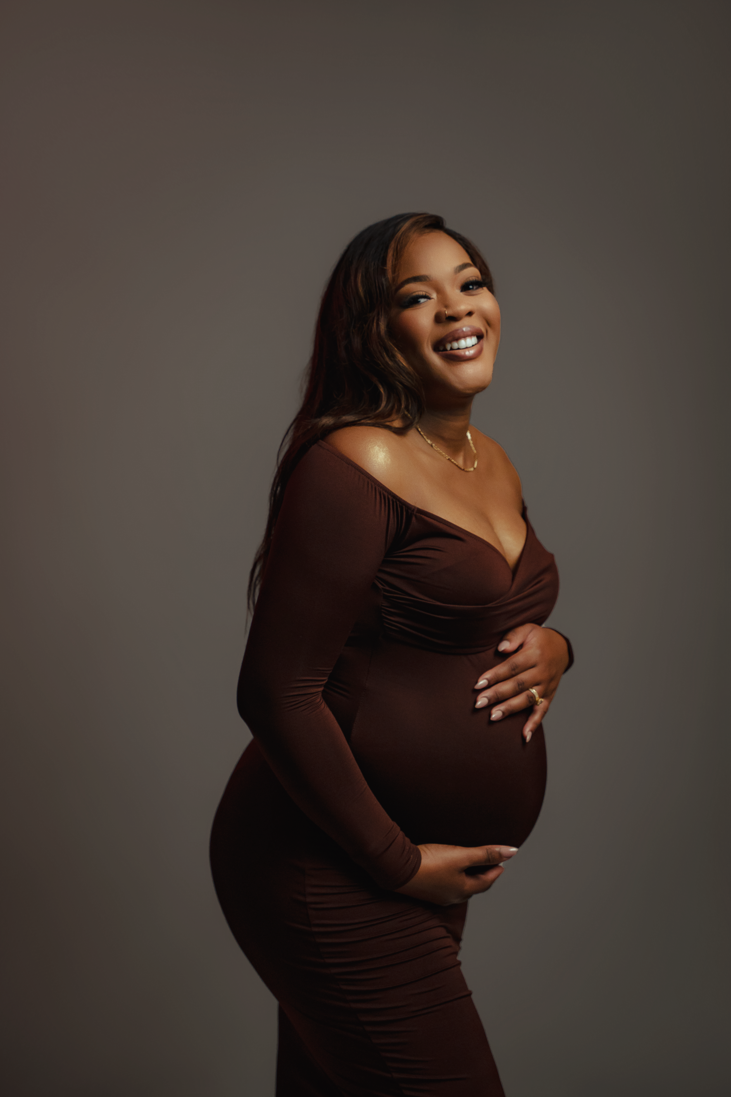 Expectant mother in brown dress smiling during maternity photoshoot.