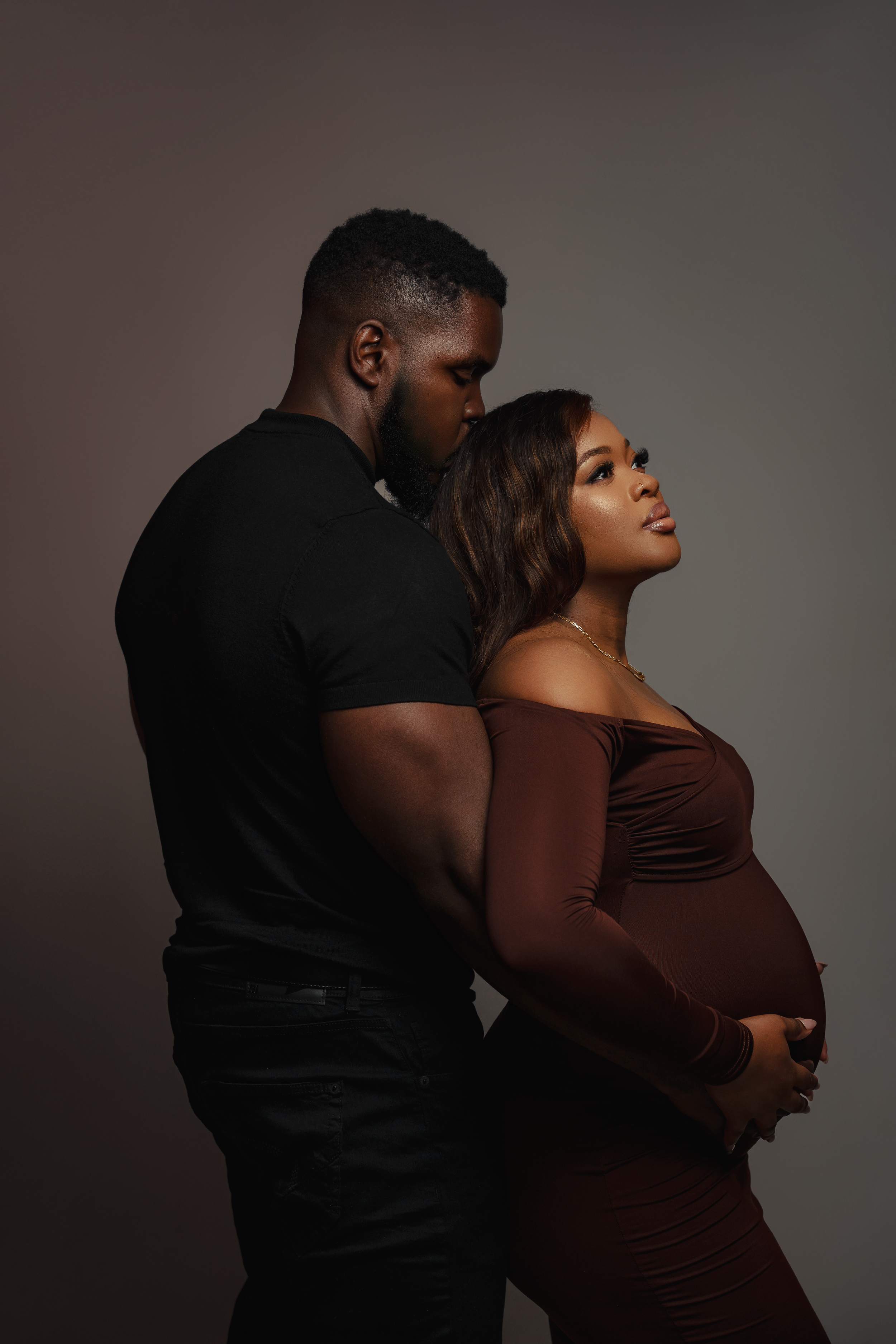 Intimate maternity portrait of couple in dark clothing against moody background.