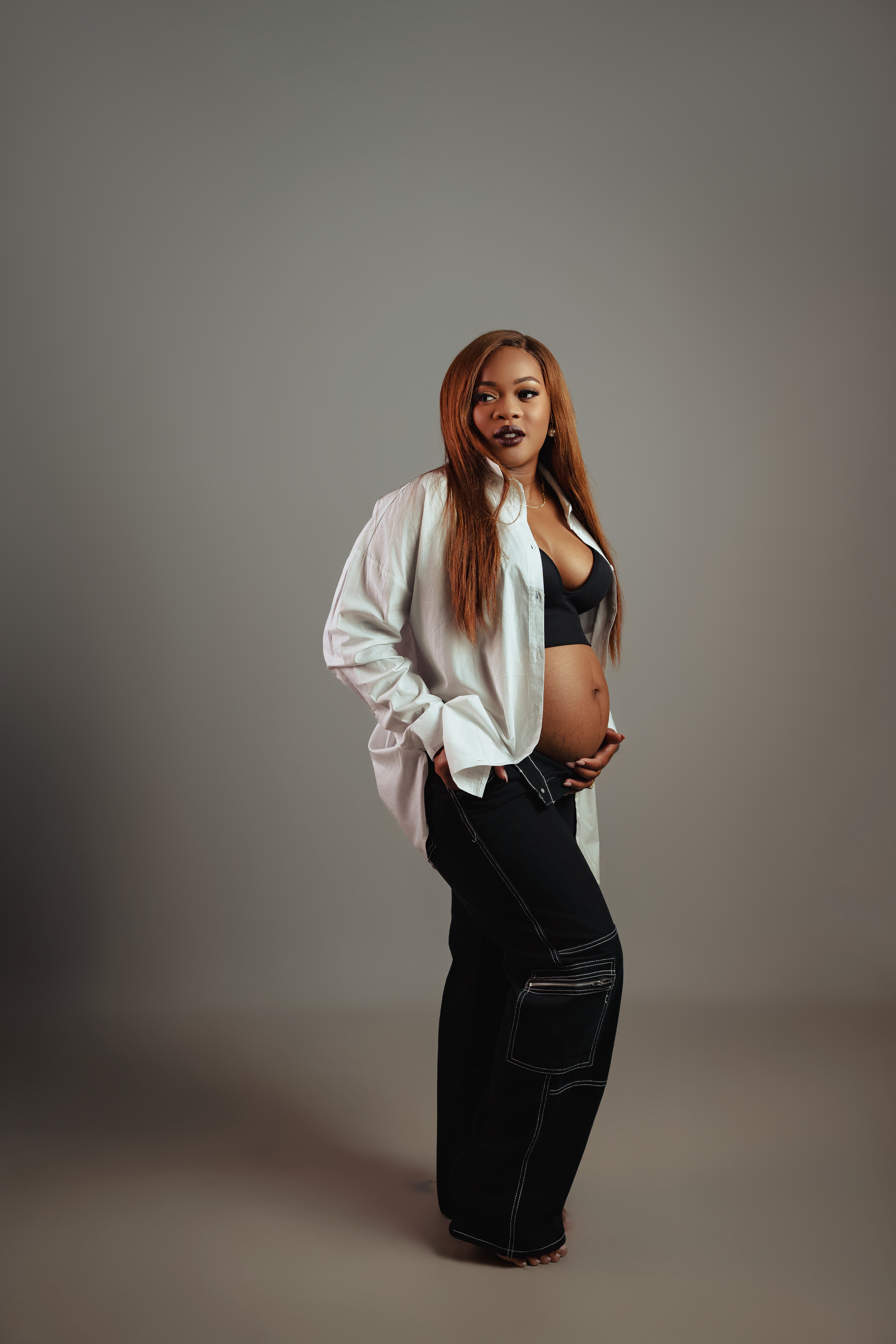 Professional maternity photoshoot featuring casual white shirt and black pants against neutral background.