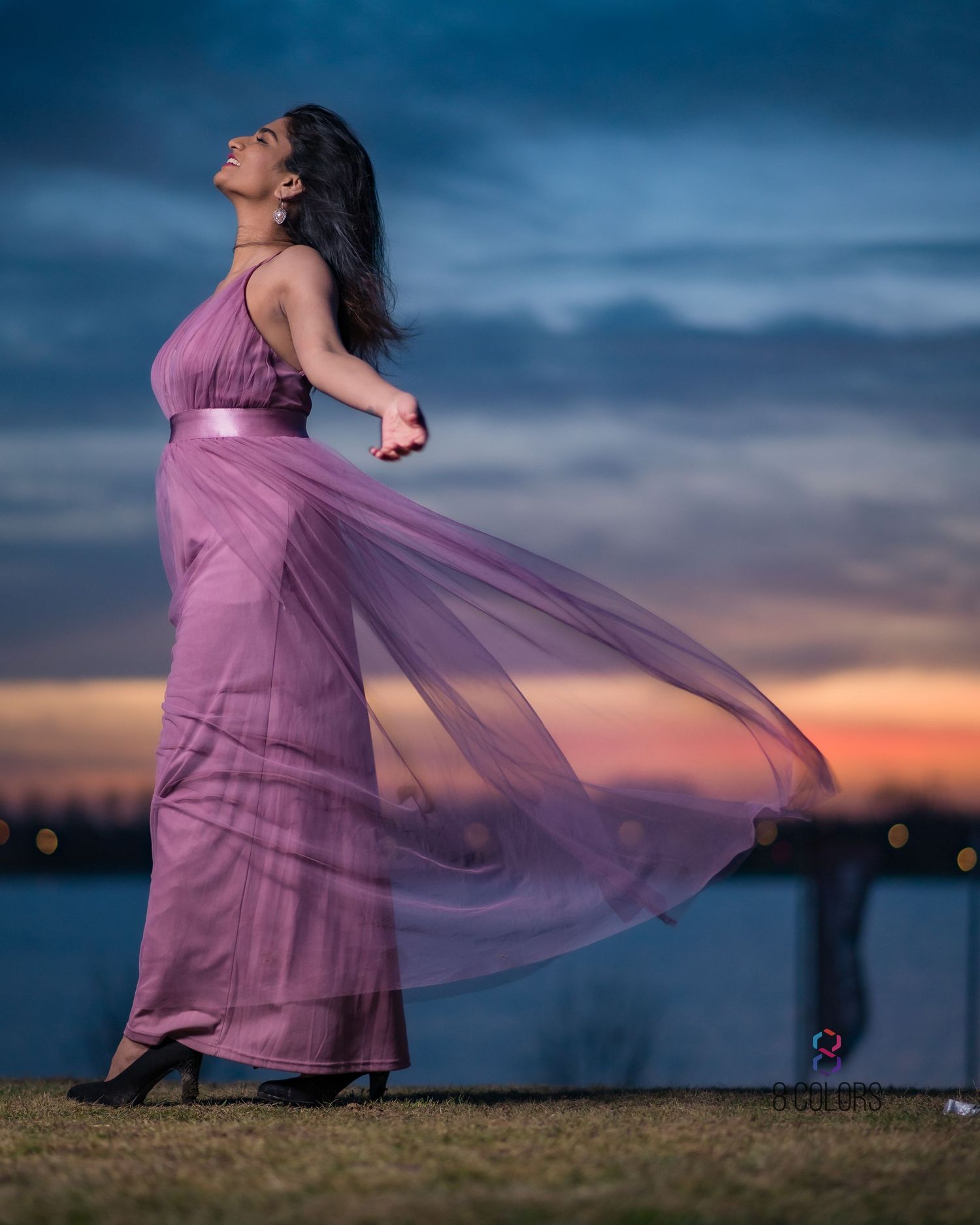 A billowing mauve dress flows in the wind during golden hour by the water's edge.