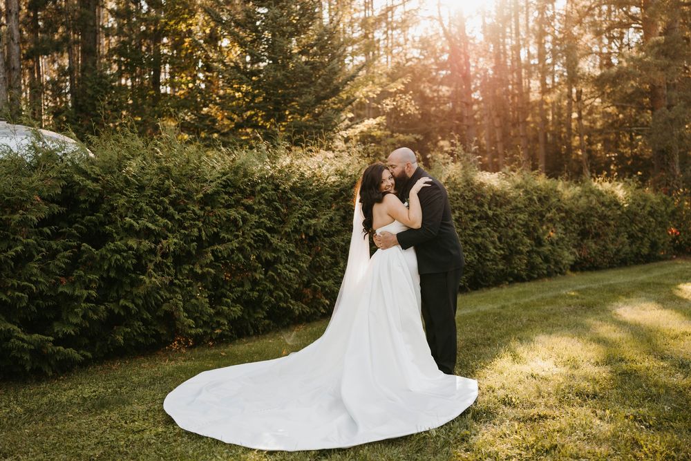Bride and groom share an intimate moment on a lawn surrounded by tall hedges bathed in warm golden sunlight.