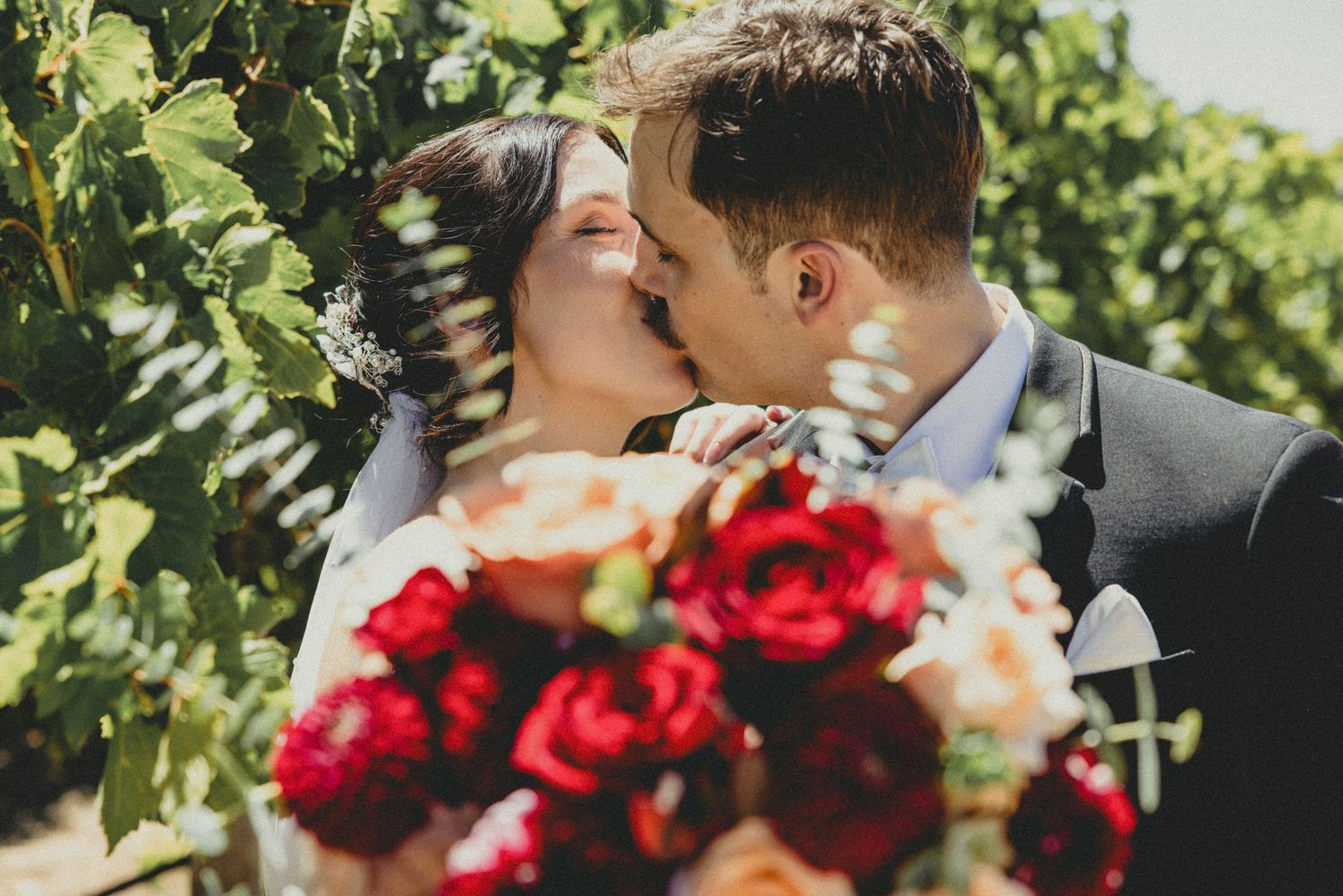 Black and white wedding ceremony photo captured through wedding guests in a forest setting.