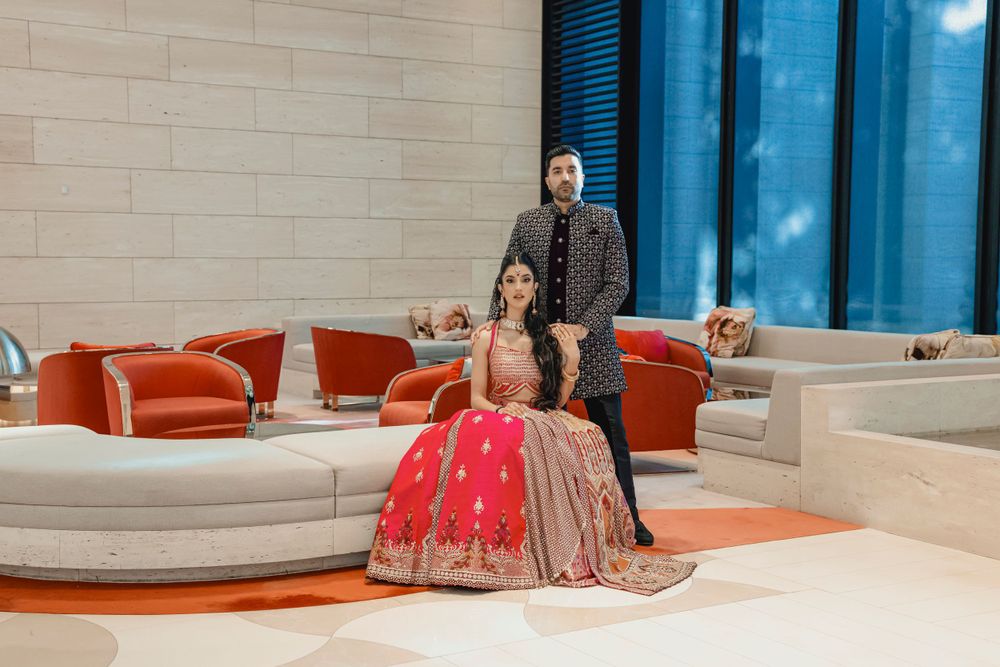 Couple in formal Indian wedding attire posing on modern white sectional sofa.