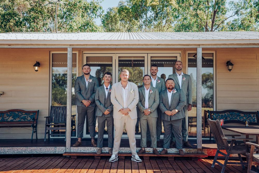 Groomsmen in grey suits posing with groom in beige on wooden deck.