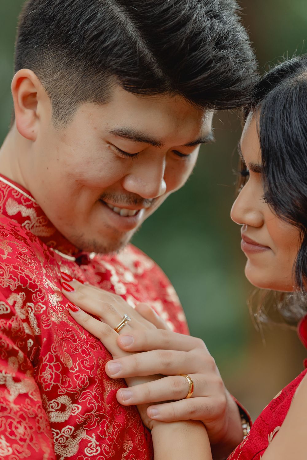 A couple in traditional red Chinese qipaos share an intimate moment while displaying their wedding rings.