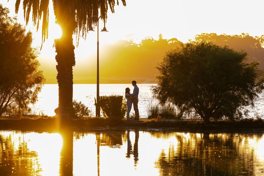 Silhouettes at sunset by a lake with palm trees and reflective water creating a golden mirror-like scene.