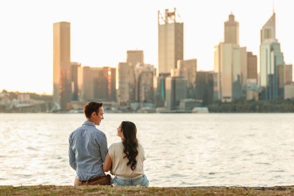 A couple sitting together at sunset overlooking the waterfront skyline of a modern city.