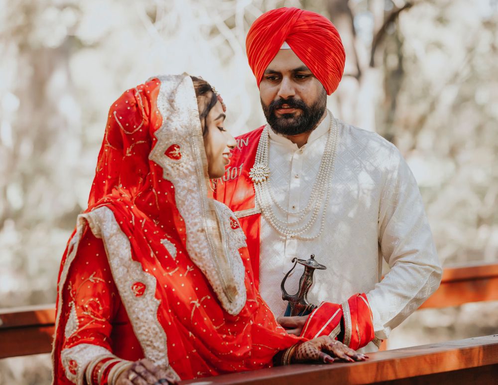 Traditional Sikh wedding couple in red and white attire sitting together outdoors.