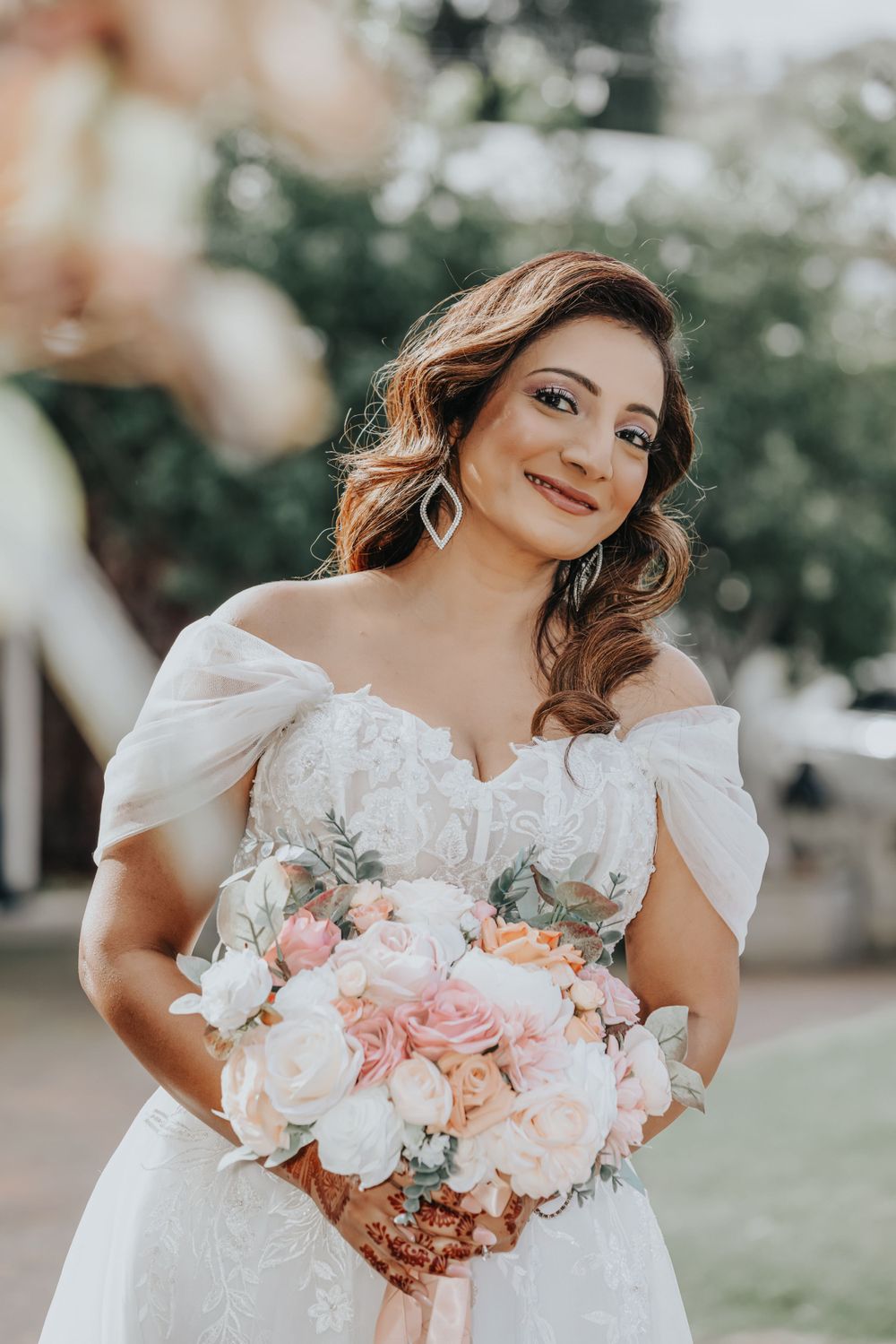 Radiant bride in off-shoulder gown holds soft pink and peach bouquet.