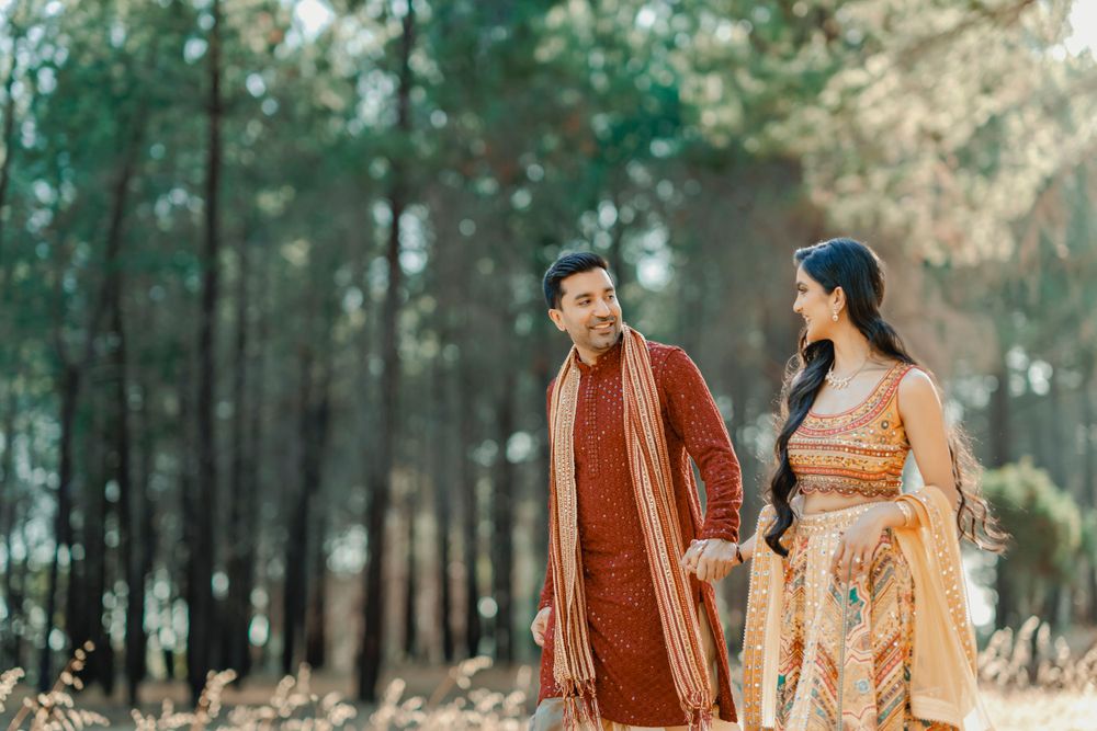 Couple in traditional Indian wedding outfits share a moment while walking through pine forest.